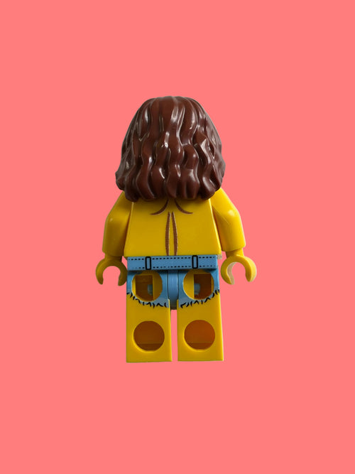 A LEGO minifigure viewed from the back, featuring brown hair, a yellow top, and blue pants, set against a plain off-white background.