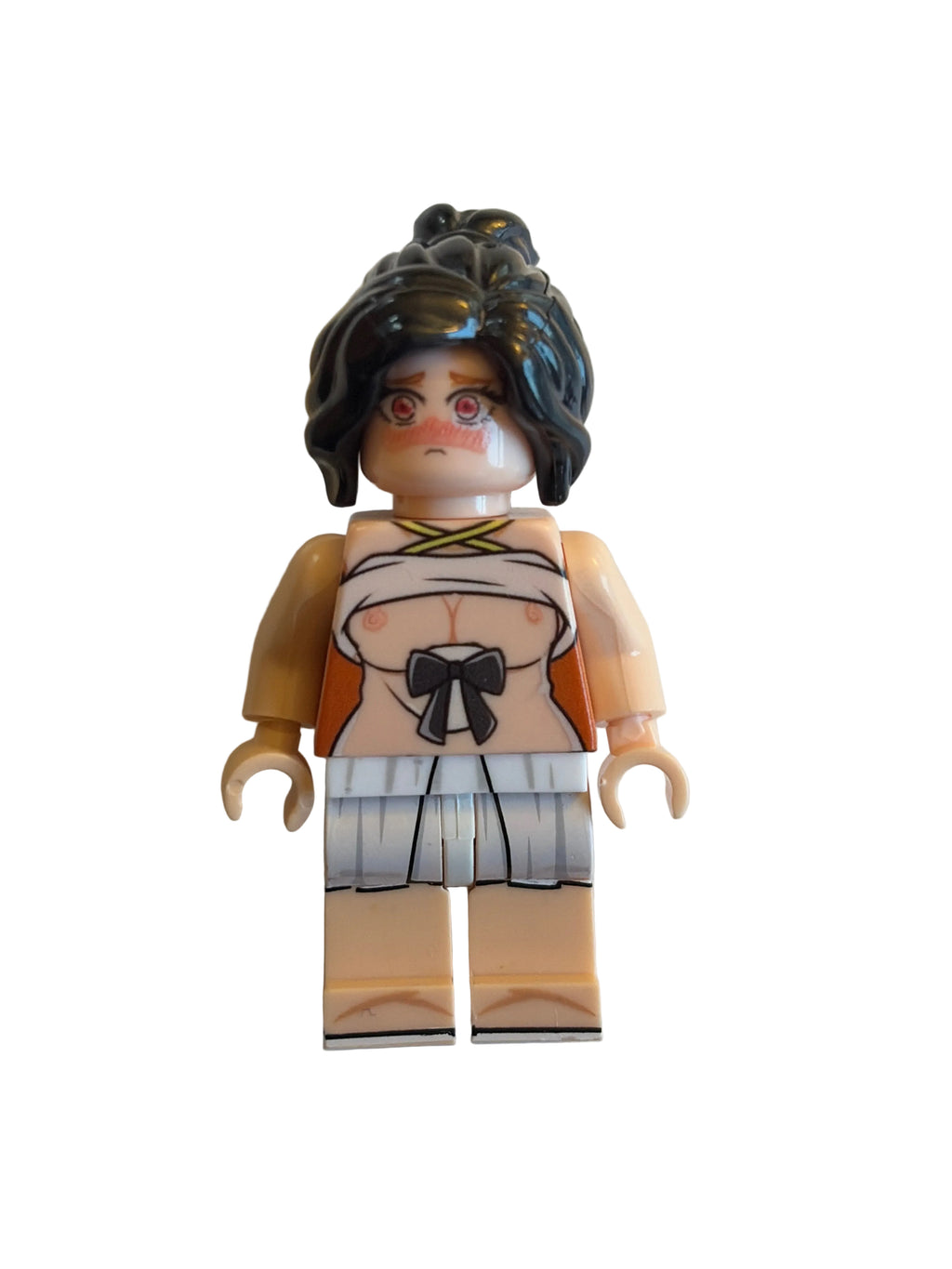 A custom-built toy minifigure with dark brown hair, a beige face, and a printed outfit featuring orange, white, and black details, lying on a plain off-white surface.