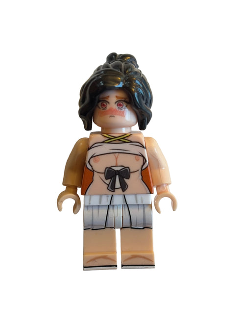 A custom-built toy minifigure with dark brown hair, a beige face, and a printed outfit featuring orange, white, and black details, lying on a plain off-white surface.