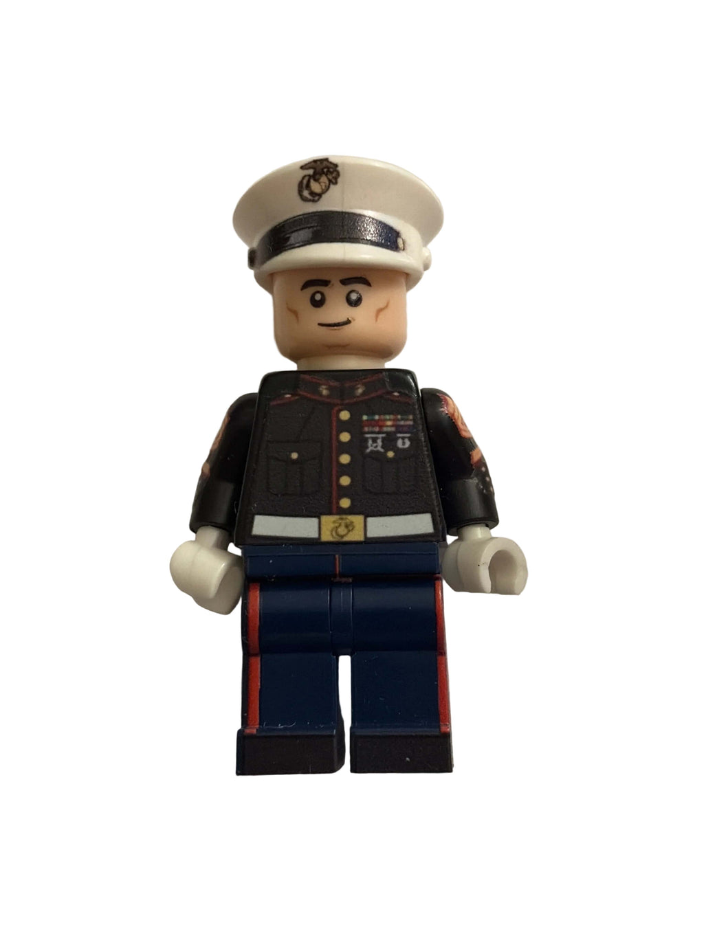 A toy United States Marine military minifigure with a beige head and hands, wearing a white service hat, a black jacket with gold buttons, and dark blue pants with red stripes, isolated on a white background.