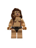 A toy minifigure of a woman with brown hair, beige skin, and a black bikini, lying on a light beige textured surface.