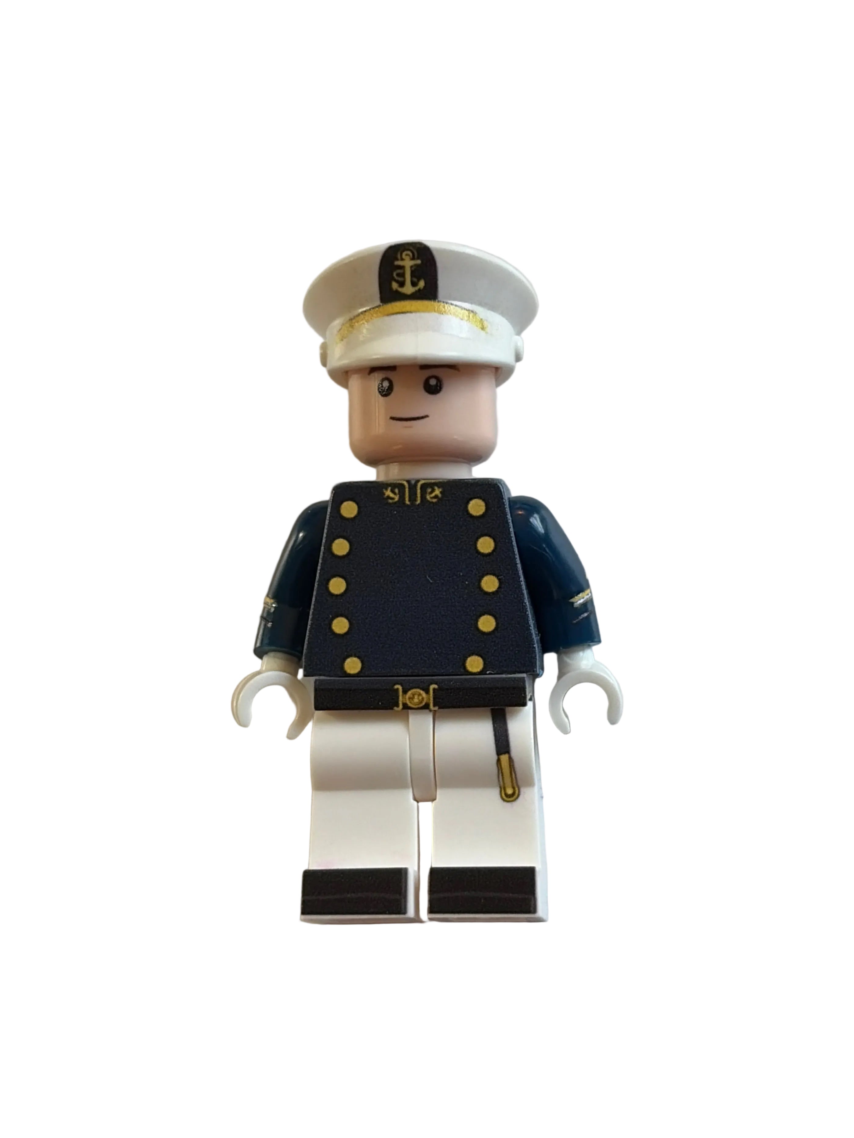 A custom-built toy minifigure resembling a LEGO brick, dressed as a navy blue officer with gold buttons, a white peaked cap, and white pants with black stripes, lying on a plain white surface.