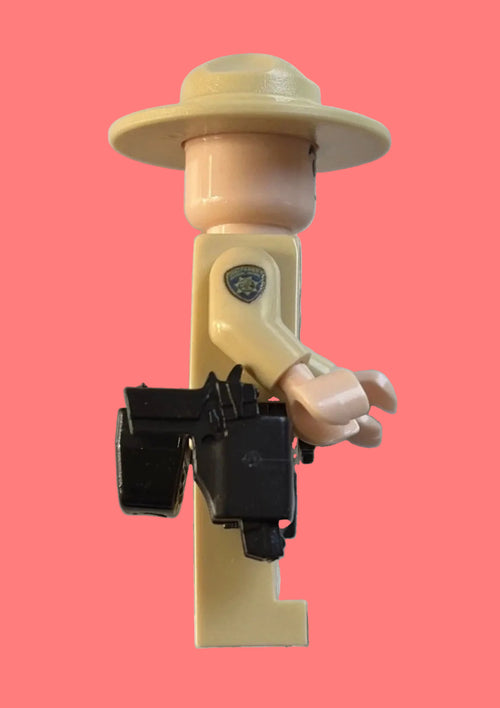A toy officer minifigure with a beige hat and torso, holding a black holster accessory, isolated on a white background.