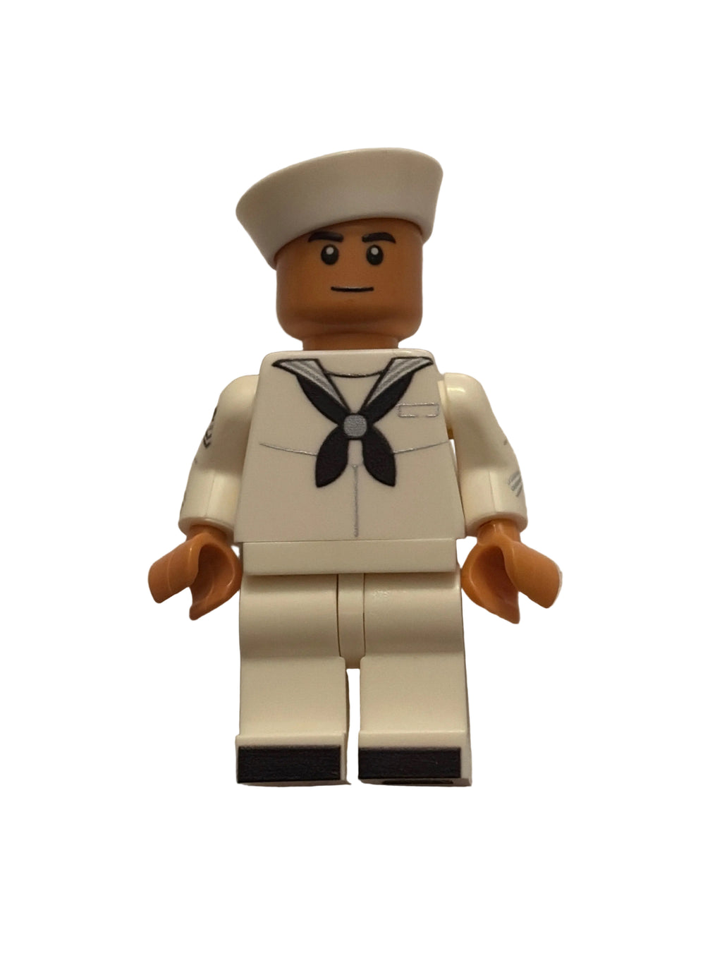 A small toy minifigure dressed in a white sailor uniform with a black bow tie and a white hat, photographed against a plain off-white wall.
