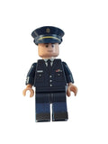 A toy minifigure dressed in a dark navy blue police uniform with a matching peaked cap, standing against a plain off-white background.