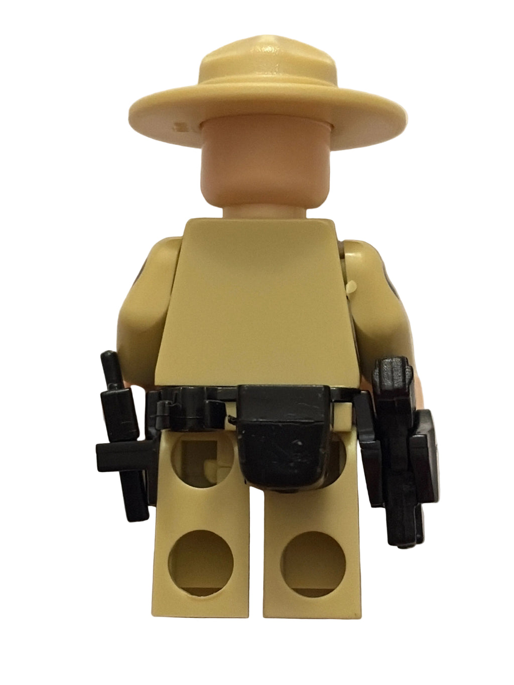 A tan and beige toy minifigure shown from the back, wearing a wide-brim hat and holding black accessories, photographed against a plain off-white background.