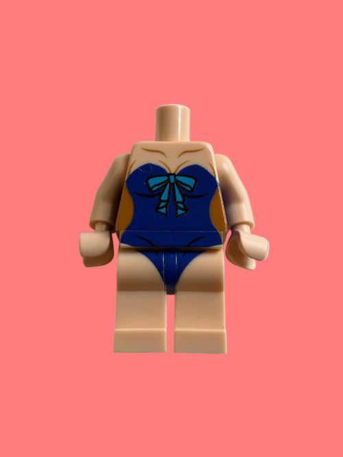 A toy minifigure torso with beige skin-tone plastic limbs and a blue swimsuit printed on the torso, featuring a teal bow detail, photographed against a plain light gray background.