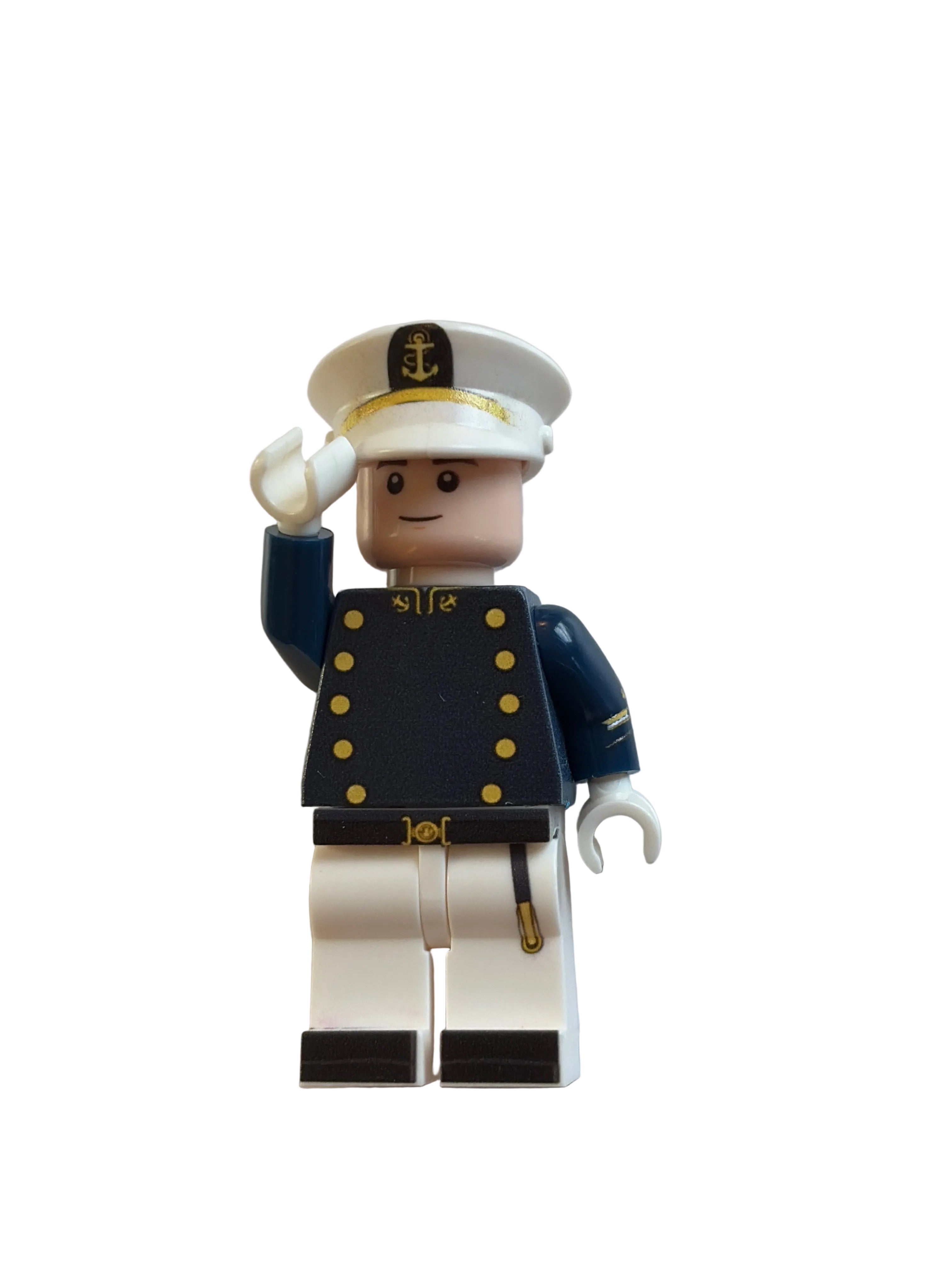 A small toy minifigure shown upside down on a plain light background. The figure has a beige head and torso, a dark navy blue jacket with gold buttons, white pants, and a white hat with a gold emblem.