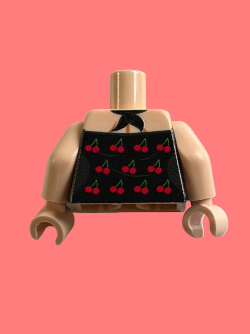 A toy minifigure torso with beige skin-tone arms and neck, wearing a black apron printed with red cherries, photographed against a plain off-white background.