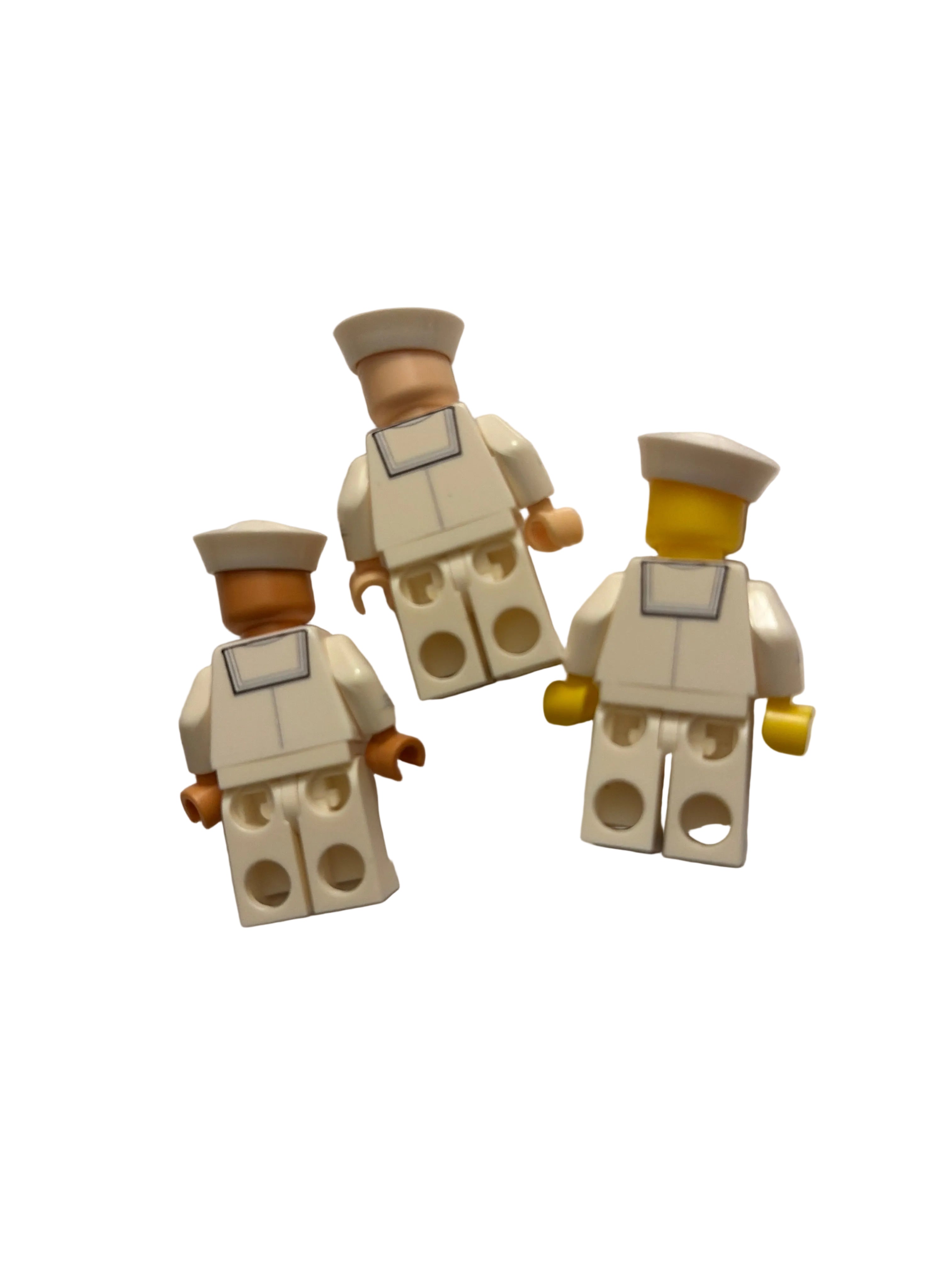 Three small toy minifigures with cream-colored bodies and hats, tan skin, and yellow hands, arranged on a white surface.