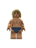A custom-built or customized toy minifigure with a beige skin tone, blonde hair, and blue shorts, photographed against a plain off-white background.