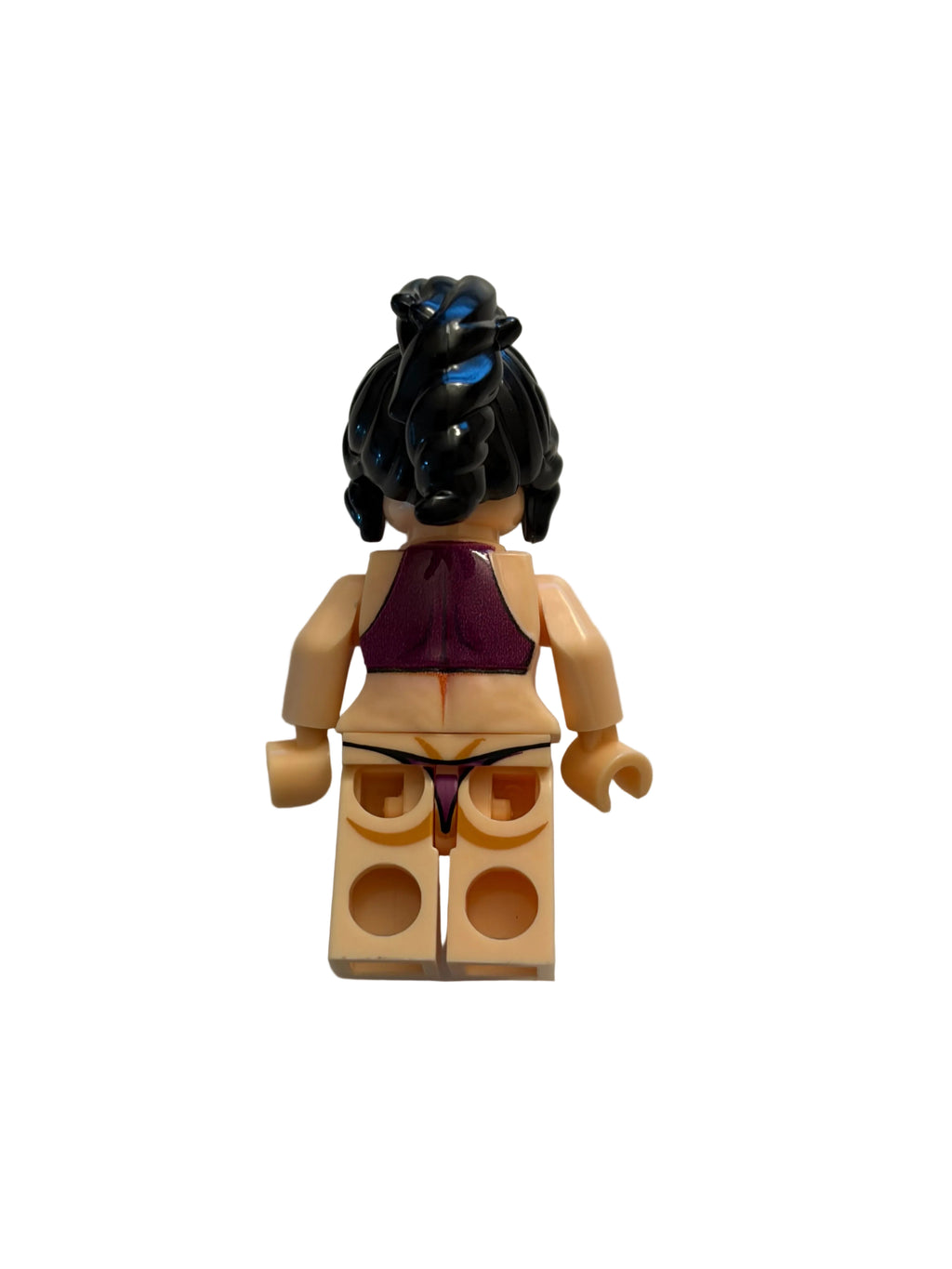 A small toy minifigure shown upside down on a plain light background. The figure has beige skin, a purple top, black hair, and a black base with blue details.