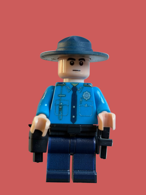 A custom-built toy minifigure of an Arkansas State Police Trooper, featuring a blue hat, bright blue shirt, dark blue pants, and black accessories, set against a plain light gray background.