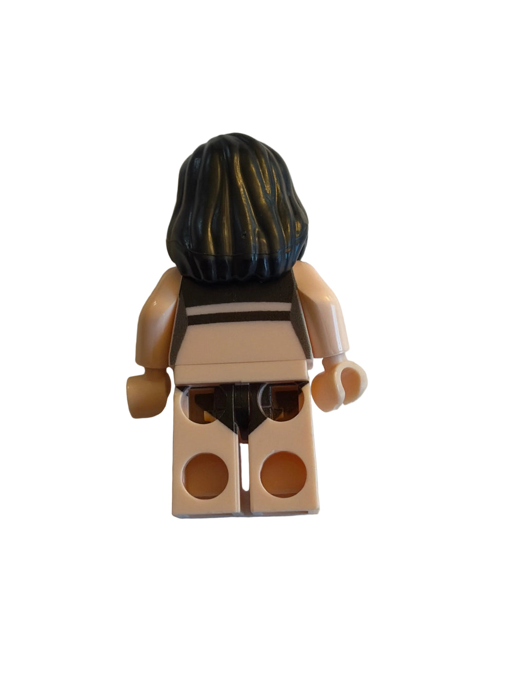 A small toy minifigure torso with black hair, beige arms and legs, and a black-and-white striped shirt, photographed on a plain light background.