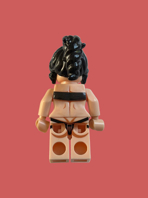A small toy minifigure torso with beige skin-tone plastic, black hair, and a black belt, photographed on a plain light background.