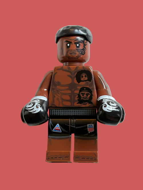 Boxer Iron Mike Tyson in his black shorts, with face and body tattoos, wearing his signature boxing gloves on a light pink background 