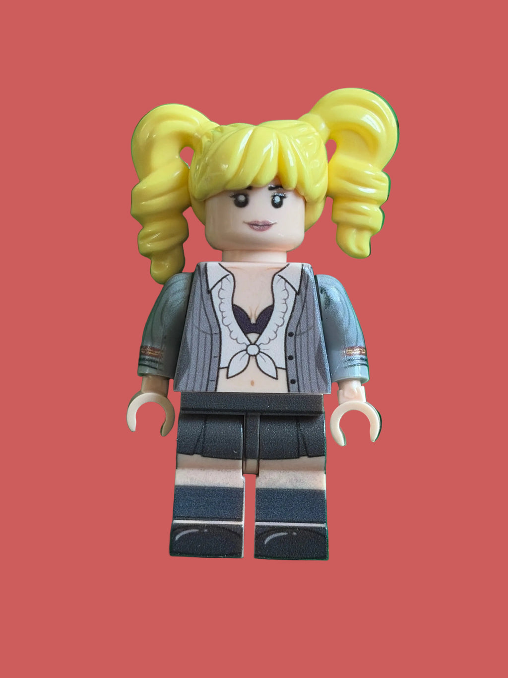 A custom-built toy minifigure of Britney Spears Oops I did it again schoolgirl outfit with yellow pigtails, a gray striped jacket, and a dark skirt, standing on a pink background.