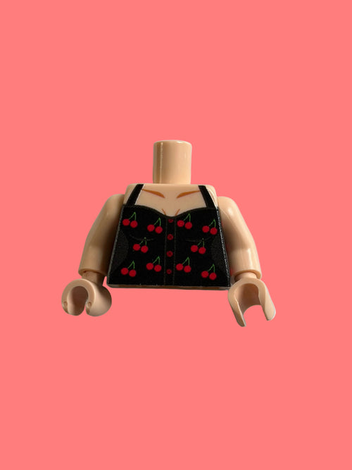 A toy minifigure torso with beige skin and printed black vest details featuring a red cherry pattern, shown against a light gray background.