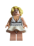 A custom-built toy minifigure of a blonde woman Marilyn Monroe with a white and black striped top and a white skirt, mounted on a beige plastic stand against a plain light gray background.