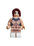 A custom-built toy minifigure with a beige plastic torso featuring explicit anatomical drawings, dark red hair, and blue eyes, standing against a plain light gray background.