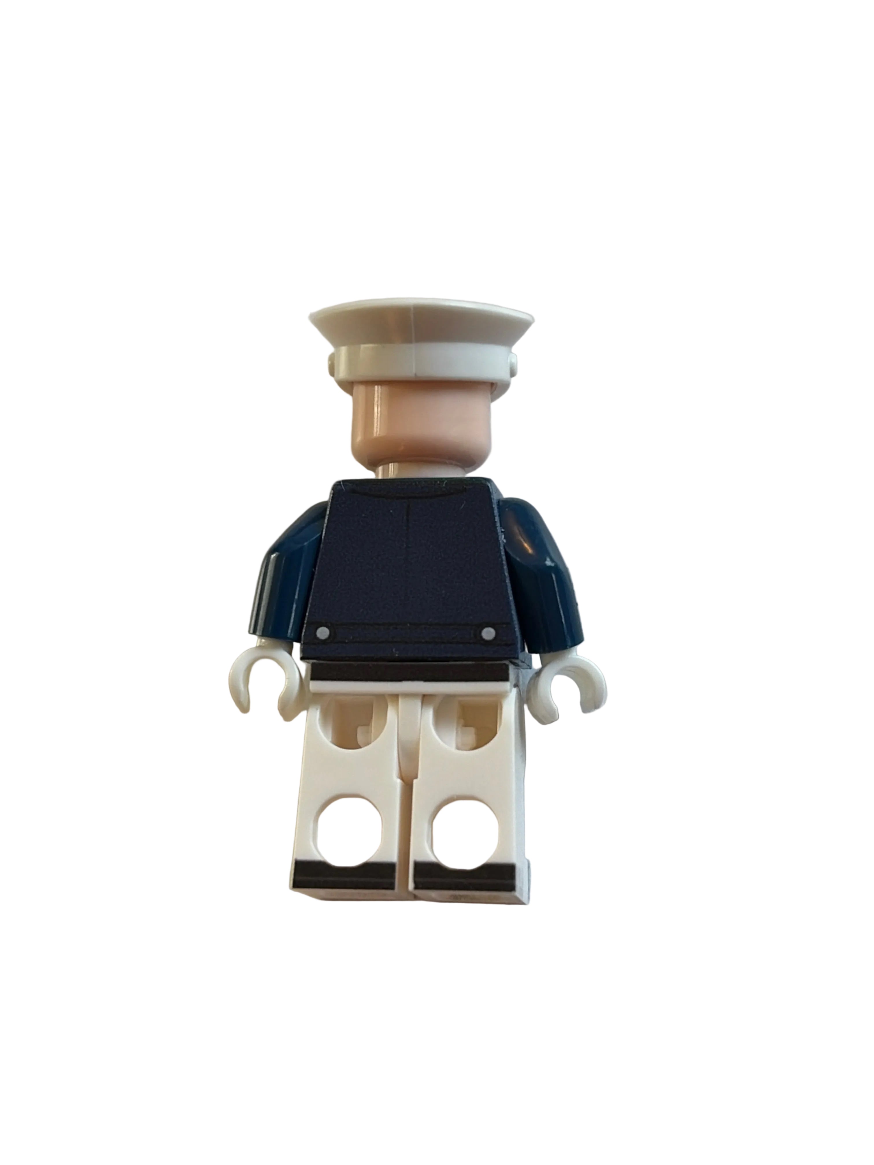 A small toy minifigure shown from the back, wearing a dark navy top, white pants, and a beige cap, photographed on a plain light background.