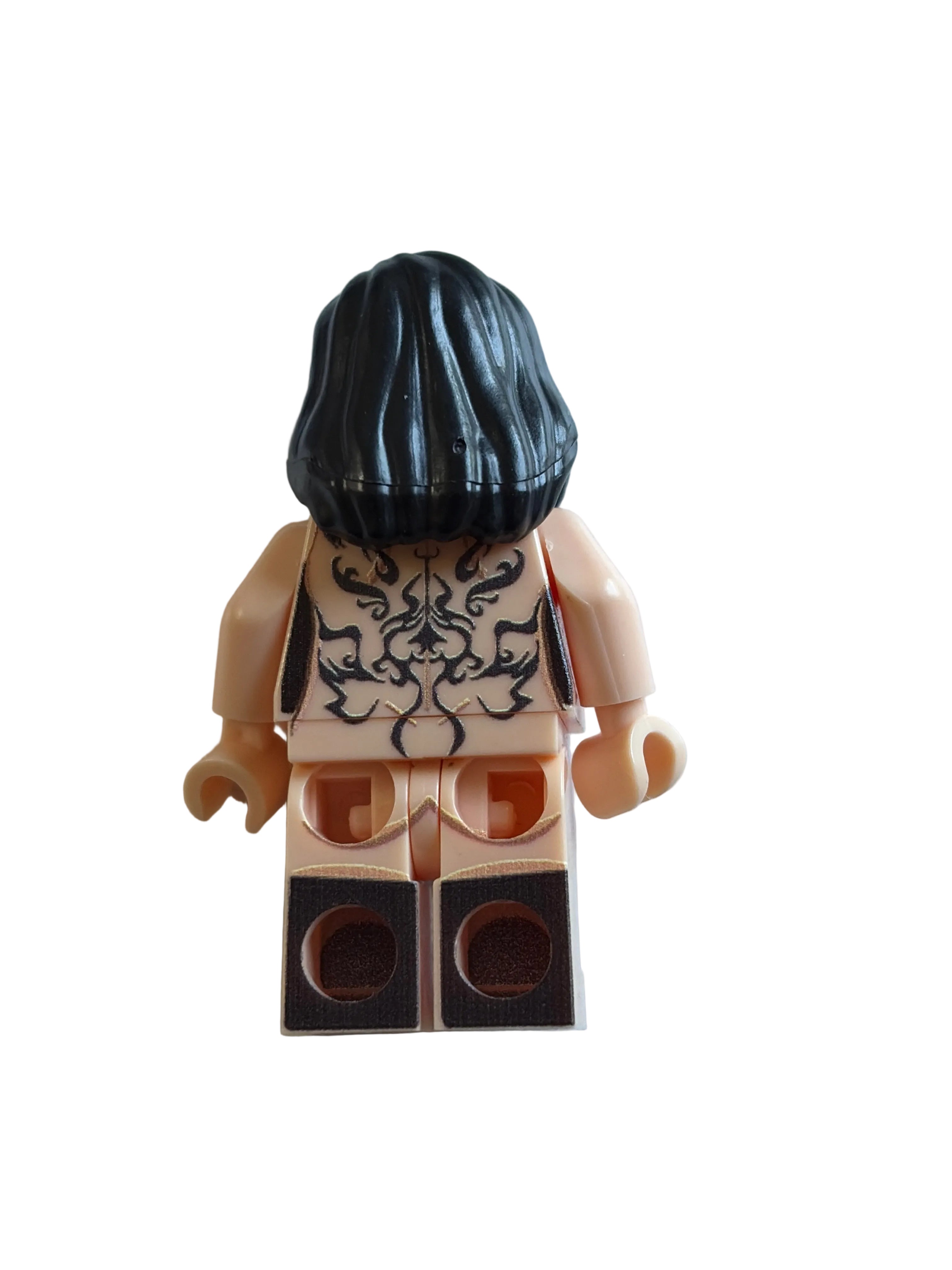 A custom-built toy minifigure torso with a black hairpiece, beige printed chest piece, and tan plastic arms and legs, photographed on a plain off-white surface.
