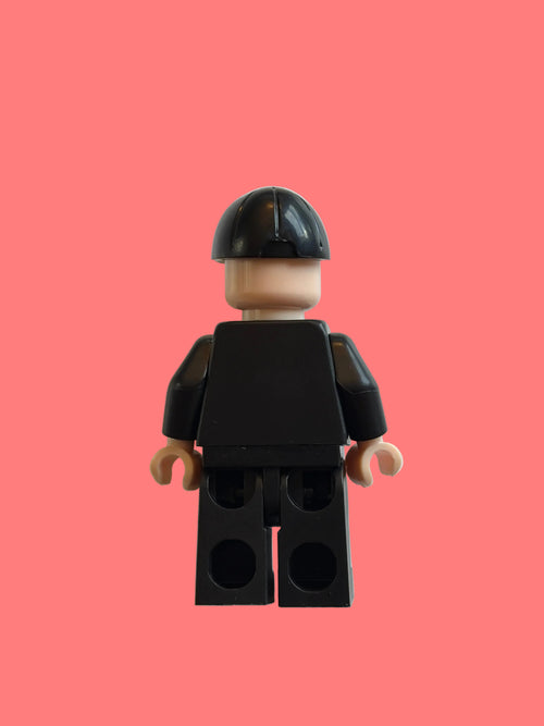 A small black toy minifigure torso with beige hands and a black-and-beige helmet, photographed on a plain off-white background.