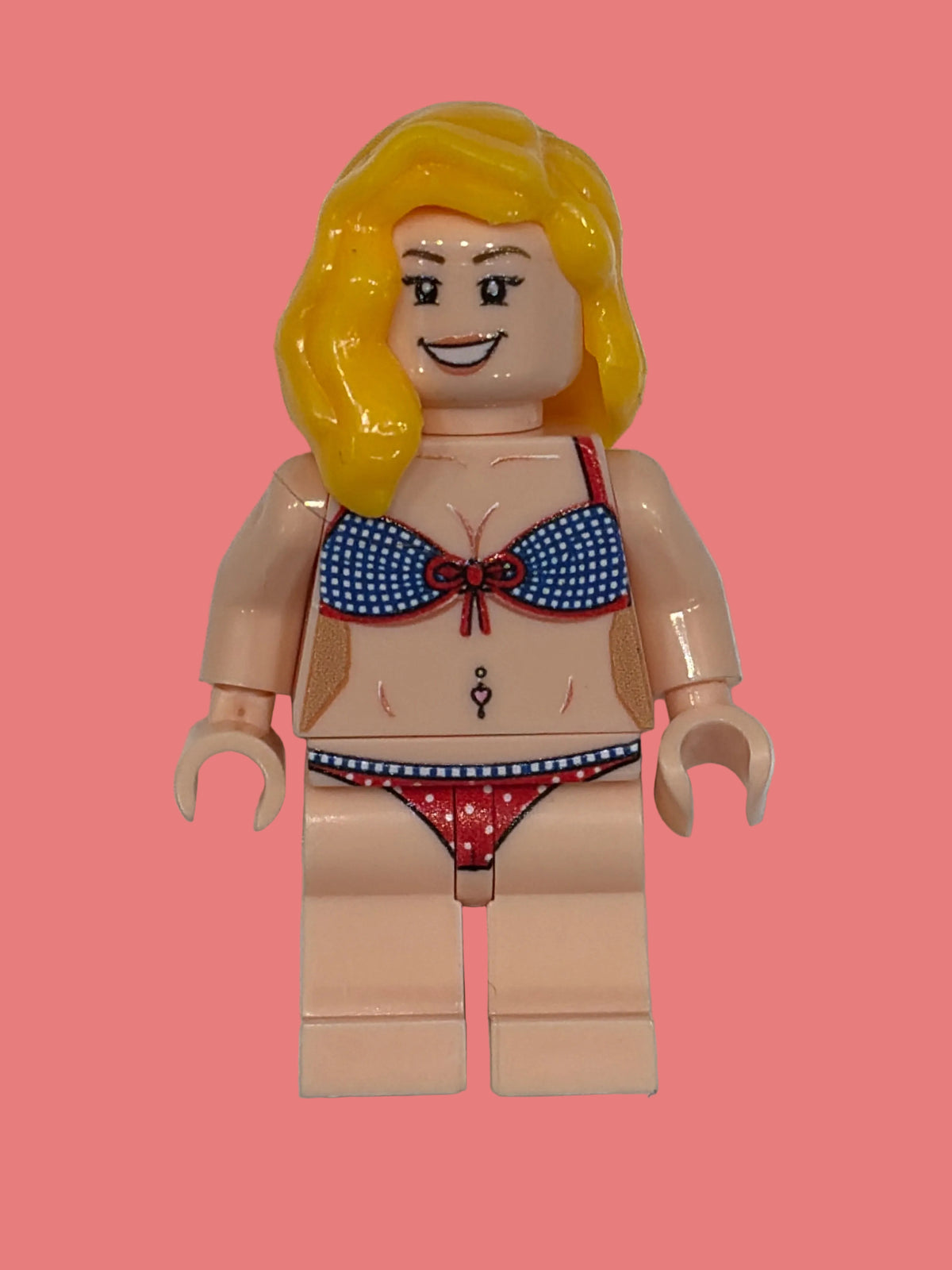 Ellie Lego style custom Minifigure in a red white and blue polka dot bikini with blonde hair smiling face on a pink background