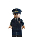 A small toy minifigure dressed in a dark navy blue police or military uniform with a matching peaked cap, photographed on a plain off-white surface.