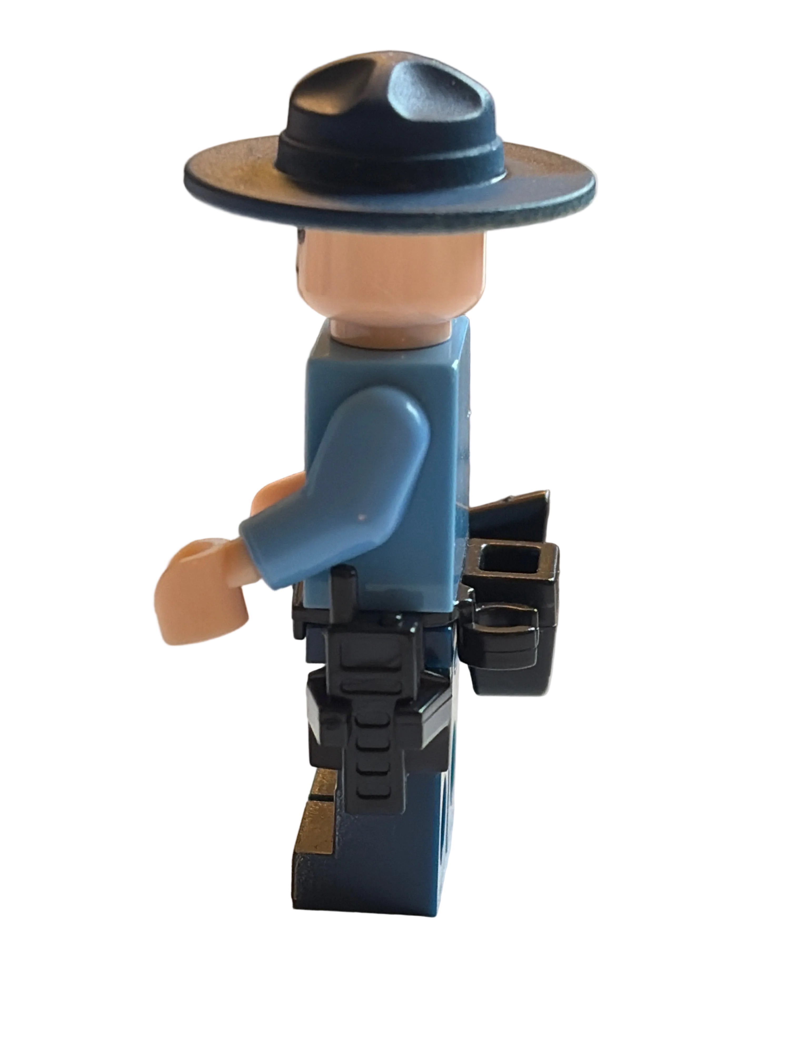A small toy minifigure with a blue torso, beige arms and hands, and a black hat, mounted on a black bracket attached to a light beige wall.
