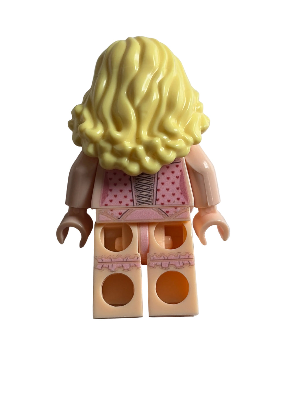 A toy minifigure torso with a large yellow wig, pink patterned dress, and beige plastic arms and legs, photographed on a plain light background.