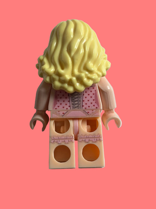 A toy minifigure torso with a large yellow wig, pink patterned dress, and beige plastic arms and legs, photographed on a plain light background.