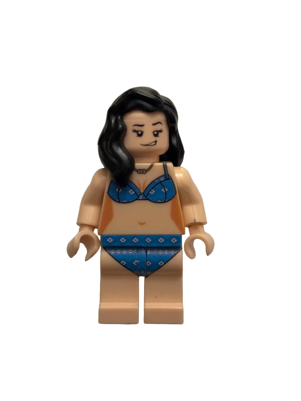 A custom LEGO minifigure of a woman with long black hair, wearing a blue patterned bikini, lying on a light gray textured surface.