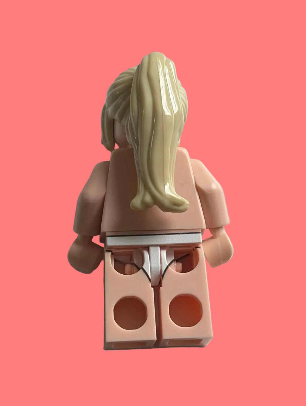 Rear view of a toy minifigure with blonde hair in a ponytail, peach skin, and white underwear, isolated on a white background.