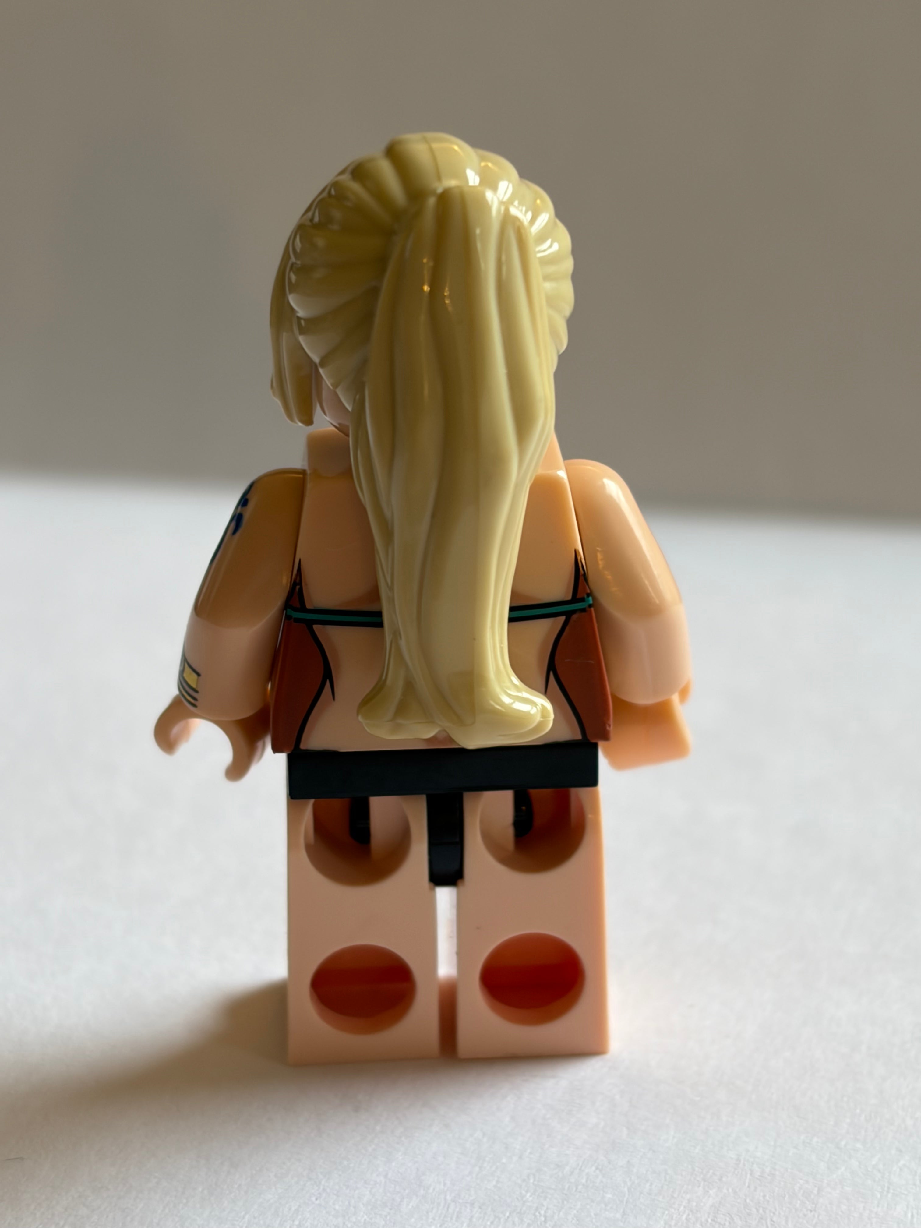 LEGO figure with blonde hair face backwards in a swimsuit on a neutral background