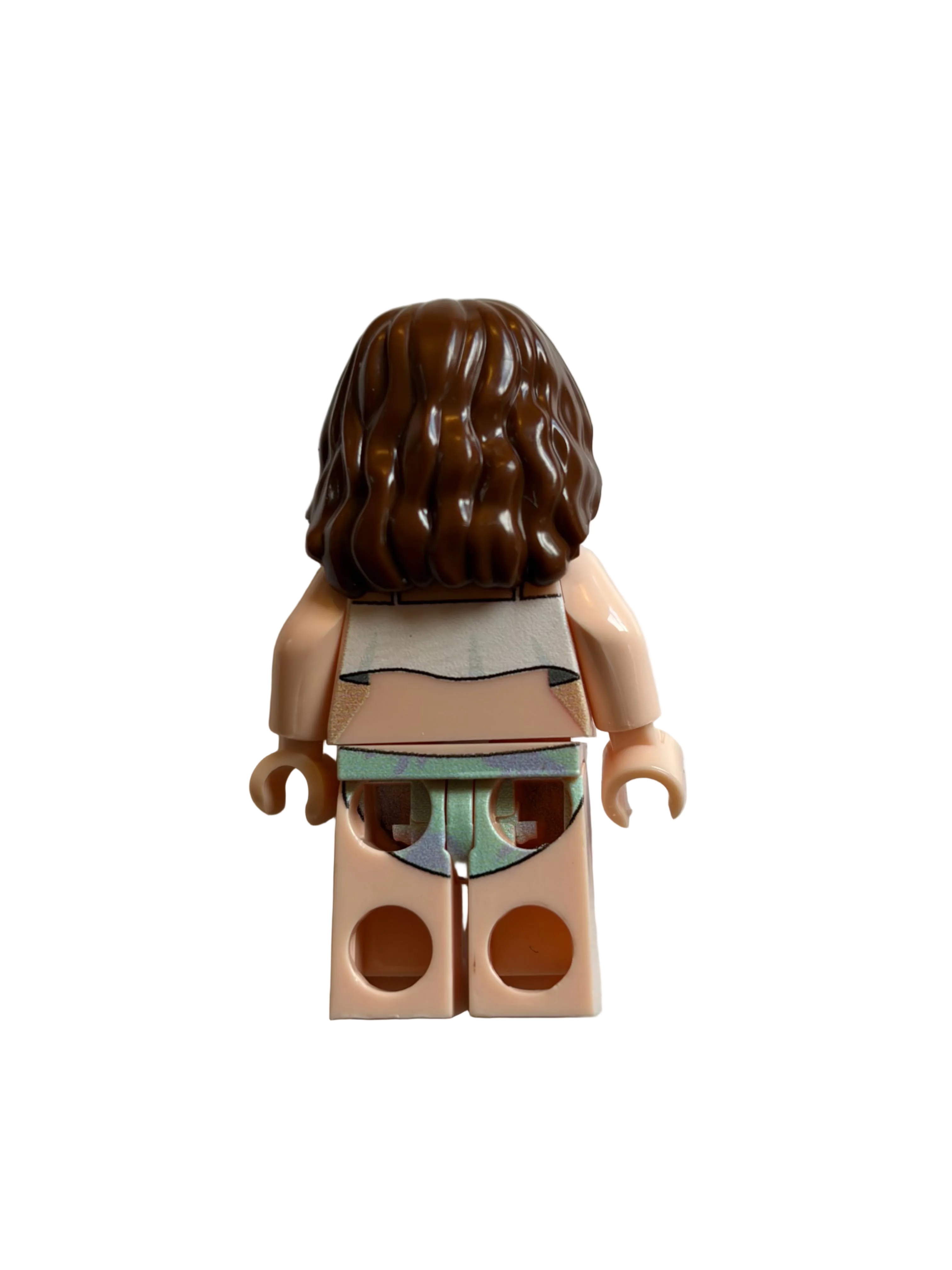 A back view of a small toy minifigure with brown wavy hair, peach skin, a white top, and a green and blue patterned skirt, standing against a plain off-white background.
