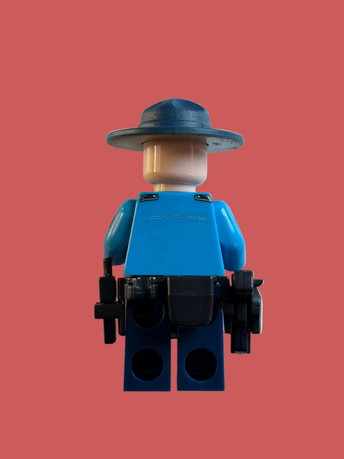 A toy minifigure shown from the back, wearing a blue shirt, dark blue hat, and black utility belt with two black guns, against a plain off-white background.