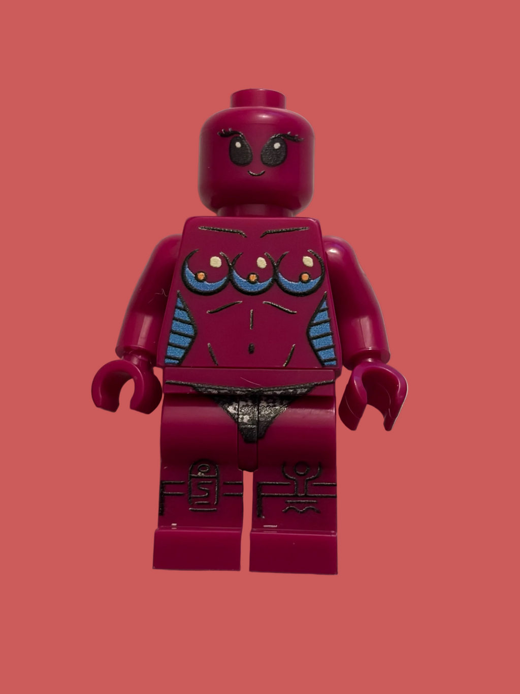 A custom-built female LEGO style minifigure in a dark magenta color, featuring a printed chest with three teardrop-shaped bra designs in blue, yellow, and white, and gray printed details on the thighs, set against a plain beige background.