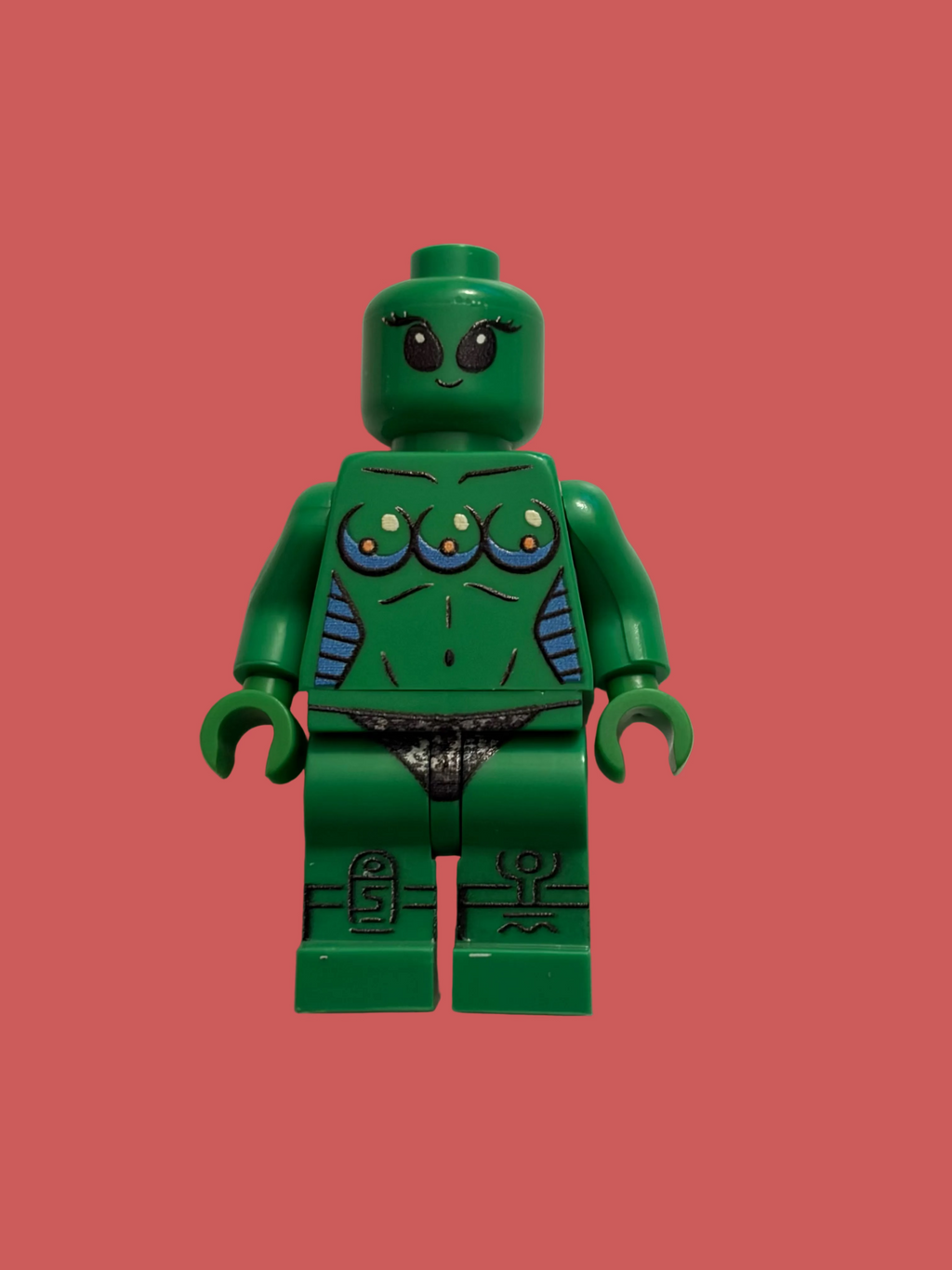A green female lego style minifigure with stylized facial features, a muscular torso, and blue patterned arm accents, standing against a plain off-white background.