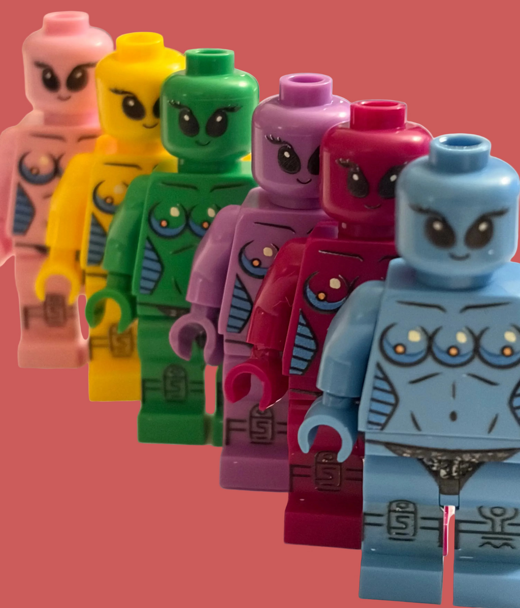 A group of colorful toy minifigures lined up in a row, featuring different body colors including pink, yellow, green, purple, magenta, and light blue, with a pink background.