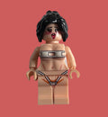 A custom-built female minifigure with black hair, a distressed face, and a beige body, wearing a silver metal collar and a black and white thong with red details, isolated on a pink background.